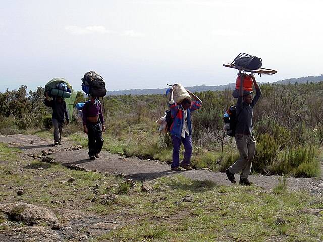 Porters carrying trekking gear on Mount Kilimanjaro trail during a guided climb"